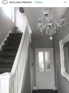 a hallway with stairs, mirror and chandelier