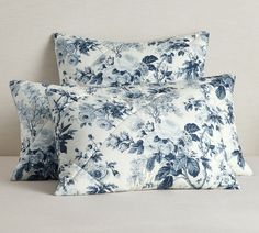 two blue and white floral pillows sitting on top of a bed next to each other