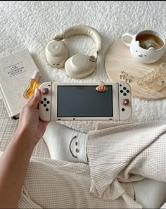 a person laying on a bed holding a nintendo wii game controller next to other items