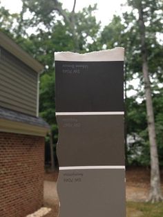 some gray and brown paint samples in front of a brick house with trees behind them