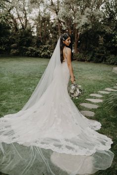 a woman in a wedding dress is standing on the grass with her veil over her head