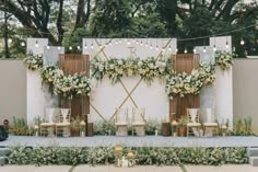 an outdoor ceremony setup with white flowers and greenery on the wall, surrounded by string lights