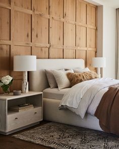 a bedroom with wood paneled walls and white bedding, along with two lamps on either side of the bed