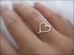 a person's hand with a heart shaped ring on their left finger, and the middle