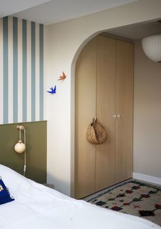 a bedroom with striped walls and white bedding has a blue pillow on the bed