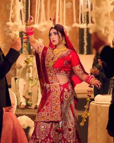 a woman in a red and gold bridal outfit is holding her hand up to the ceiling