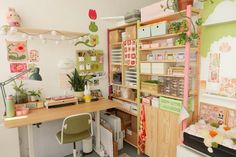 a desk with lots of items on it in a room filled with plants and decorations