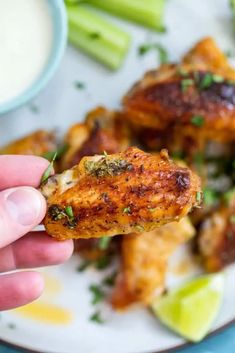 a hand holding up a piece of chicken with sauce and celery on the side