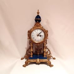 an ornate clock with blue and gold trim on it's sides, against a white background