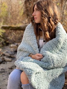 a woman sitting on the ground with her arms crossed and she is wrapped in a blanket