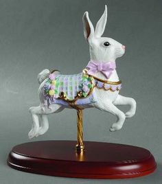 a figurine of a white rabbit wearing a pink bowtie on a wooden base