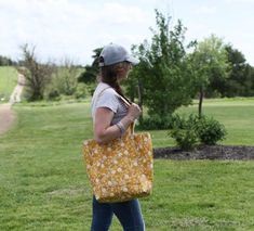 a woman carrying a yellow bag walking across a lush green field