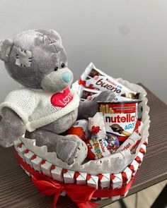 a teddy bear sitting in a basket filled with candy and snacks on top of a table