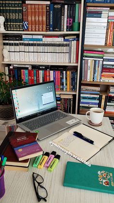 an open laptop computer sitting on top of a wooden desk next to books and glasses