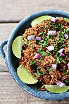 a blue bowl filled with shredded meat and garnished with cilantro, onion, and lime wedges