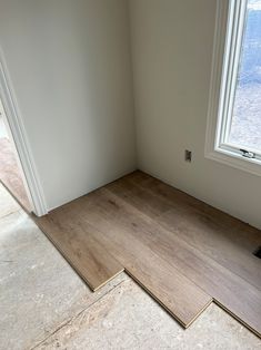 an empty room with hard wood flooring next to a window in the corner,