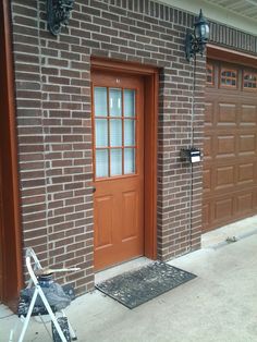 a brown door with two windows and a black mat on the sidewalk next to it