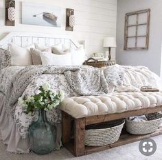 a bed with white sheets and pillows in a bedroom next to a table with baskets on it