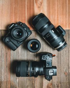 two cameras sitting next to each other on top of a wooden floor with the lens attached