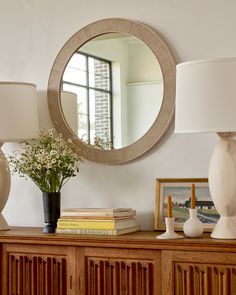 there is a mirror on the wall next to a dresser with flowers and books in it