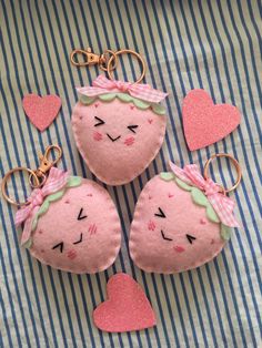 three pink stuffed strawberrys with hearts on a blue and white striped cloth covered surface