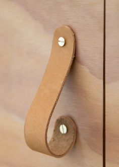 a brown leather handle on a wooden cabinet with two white knobs and a round hole in the middle