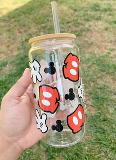 a hand holding a mickey mouse tumbler with straws in it on the grass