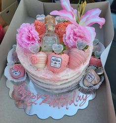 a birthday cake decorated with pink flowers and perfume bottles in a box on a table