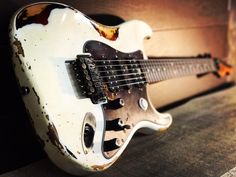 an old white electric guitar sitting on top of a wooden floor next to a wall