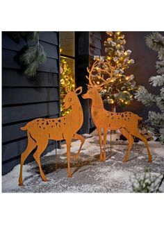 two wooden deer standing in the snow next to a christmas tree with lights on it