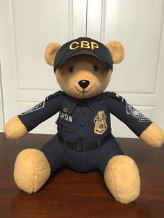 a teddy bear dressed in a police uniform sitting on a wooden table next to a door