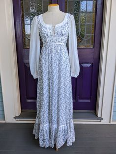 "Beautiful 1970s Gunne Sax dress in a cotton voile print of tiny purple rosebuds with green leaves and tendrils on a white background. The bodice laces up corset style, and it's trimmed in white lace with satin ribbons. The long full sleeves are in white voile dotted Swiss with lace trim on the cuff ends. The skirt is very full, and the dress is in excellent condition. It has a lovely, delicate ethereal fairy vibe. It's a little small across the back for my size 8 dress form, so it's just pinned Green Gunne Sax Dress, Spring Prairie Dress For Gatherings, Fitted Prairie Dress For Gatherings, Fitted Vintage Victorian Dress With Square Neck, Fitted Empire Waist Prairie Dress In Cottagecore Style, Fitted Prairie Dress In Cottagecore Style For Gatherings, Fitted Cottagecore Prairie Dress With Empire Waist, Fitted Victorian Dress With Square Neck, Cottagecore Fitted Prairie Dress For Gatherings