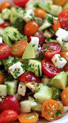 a white bowl filled with cucumber, tomato and avocado salad on top of a wooden table