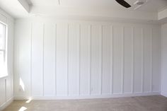 an empty room with white paneling and a ceiling fan