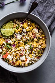 a white bowl filled with corn salad next to a lemon wedge and some purple flowers