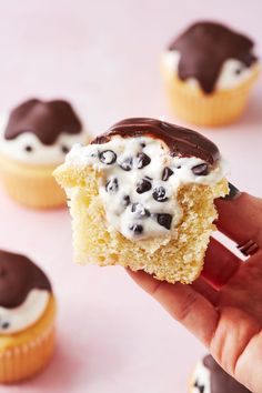 a hand holding a half eaten cupcake with chocolate chips and cream