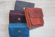 three different colored leather wallets sitting on top of a wooden table next to each other