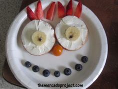 a white plate topped with fruit and two bananas on top of each other in the shape of a face