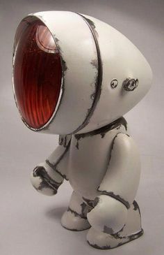 a small white toy with a red light on it's head and legs, standing in front of a gray background