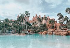 a large pool surrounded by palm trees next to tall buildings and water features in the background