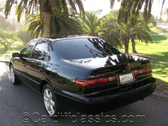 a black car is parked on the side of the road in front of some palm trees