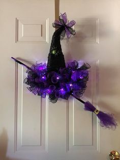 a purple witch hat hanging on the front door with a broom and light up eyes