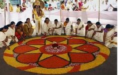 a group of people sitting in front of a large flower arrangement on the ground at a festival