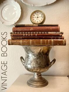 there is a silver vase with books on it and a clock in the back ground