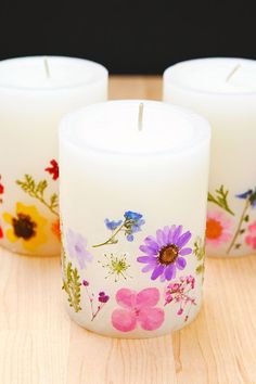 three white candles sitting on top of a wooden table next to each other with flowers painted on them