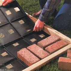 a man is placing bricks into an outdoor fire pit with grass and rocks in the background