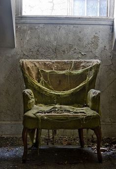 an old chair sitting in front of a window with a tarp covering it's back