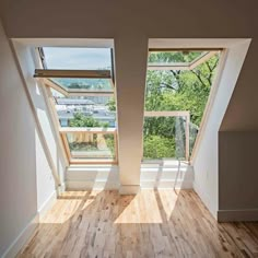 an empty room with wooden floors and two windows on each side, looking out onto the trees outside