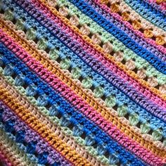 a crocheted blanket with multicolored stripes is shown in close up view