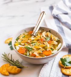 a white bowl filled with chicken noodle soup next to crackers